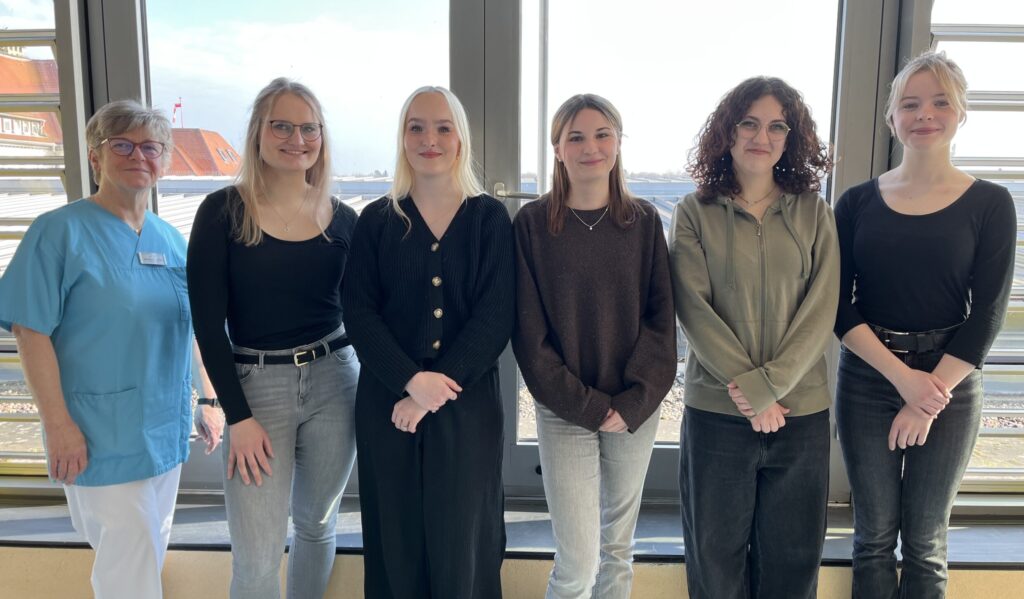 Fünf Schülerinnen der PFK-Winterklasse stehen zusammen mit Praxisanleiterin Ulrike vor einem großen Fenster