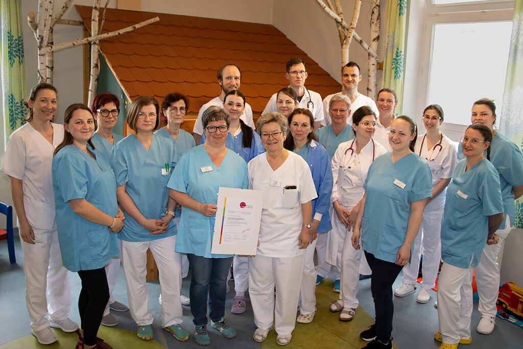 Das Team der Klinik für Kinder- und Jugendmedizim um Chefärztin MUDr. Heike Reck steht im Spielzimmer mit der neuen Auszeichnung