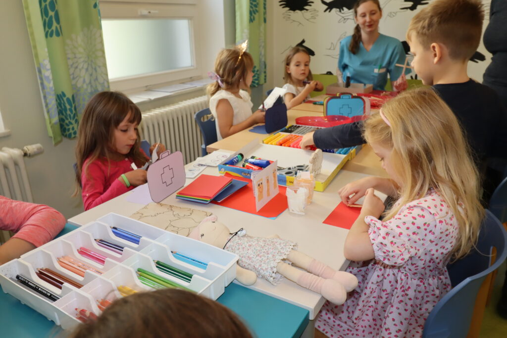 mehrere Kinder sitzen an einem langen Tische und malen und bastelt